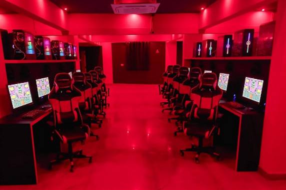 A gaming cafe lit in red, with PCs and gaming chairs along both walls