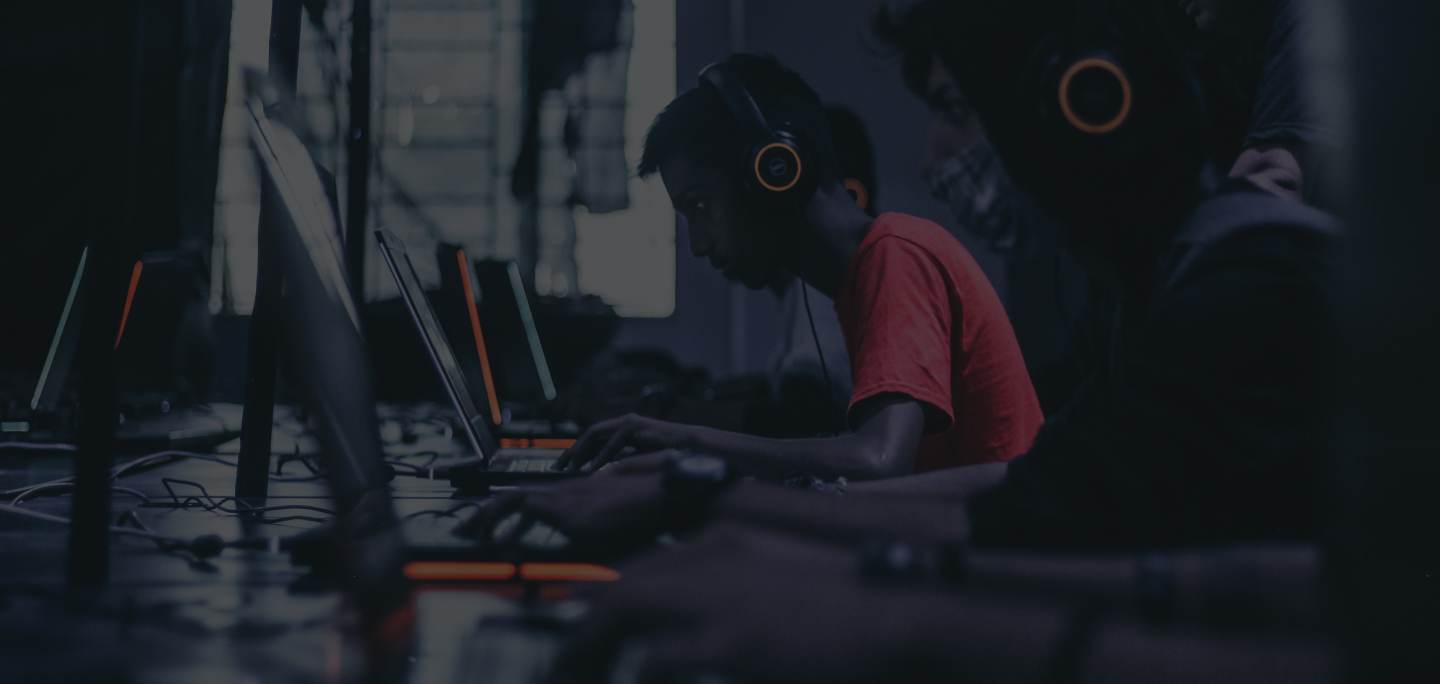 A gamer wearing headphones, playing at a PC in a dim gaming cafe