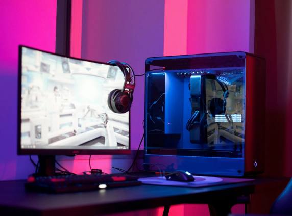 A custom gaming PC with a glass side panel next to a curved monitor, lit in pink and blue